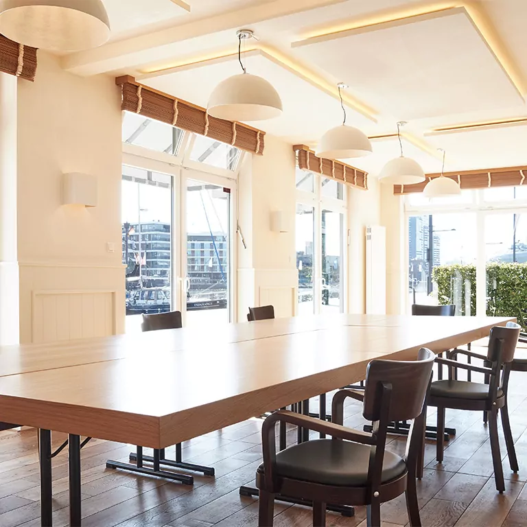 Heller Konferenzraum mit großem Holztisch, eleganten Stühlen und großen Fenstern mit Blick auf die Stadt.
