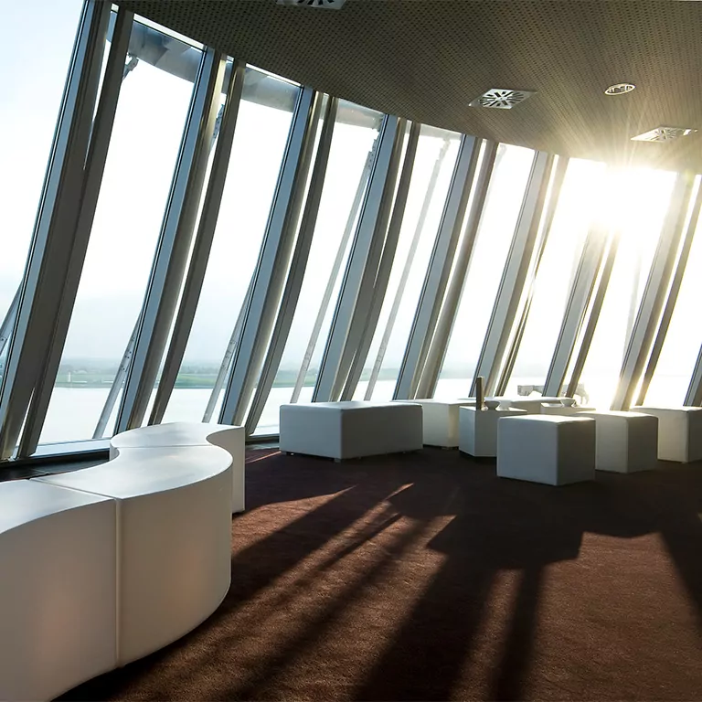 Moderner Tagungsraum im ATLANTIC Hotel Sail City mit weißen Möbeln, großen Fenstern und Blick auf Flusslandschaft bei Sonnenuntergang.