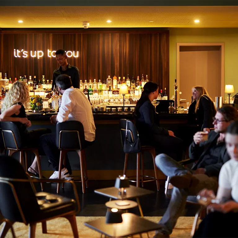 Gemütliche Hotelbar mit Menschen, die an einem Tresen sitzen, Getränke genießen und sich unterhalten.